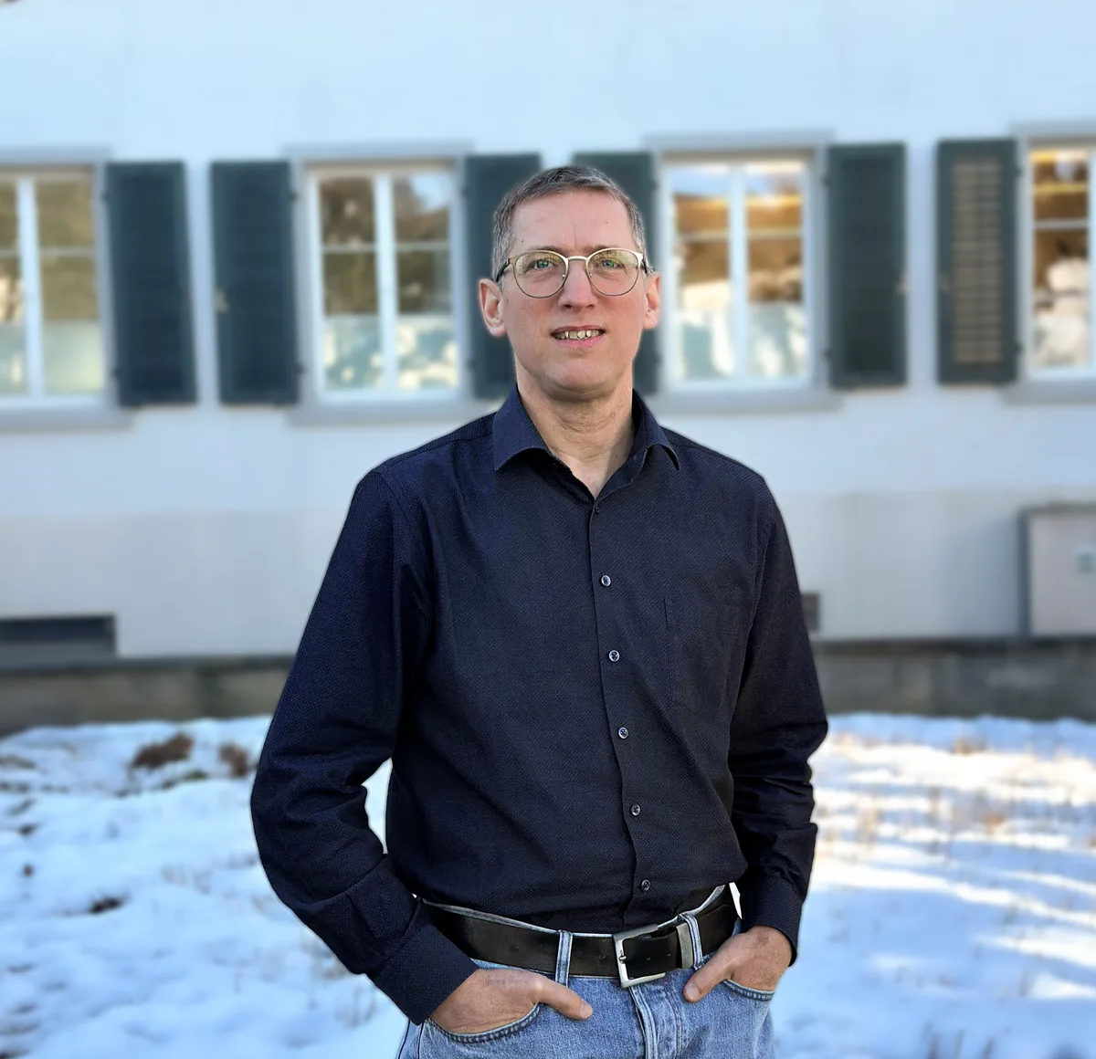 Ein Mann steht vor einem Gebäude, beide Hände stecken in der Hosentasche.